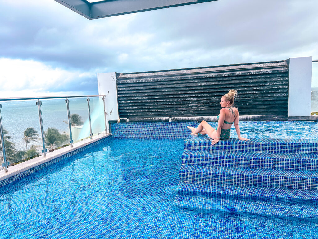 blonde-woman-in-emerald-green-bathing-suit-sitting-in-rooftop-pool-at-the-watermark-ambergris-caye-belize-hotel