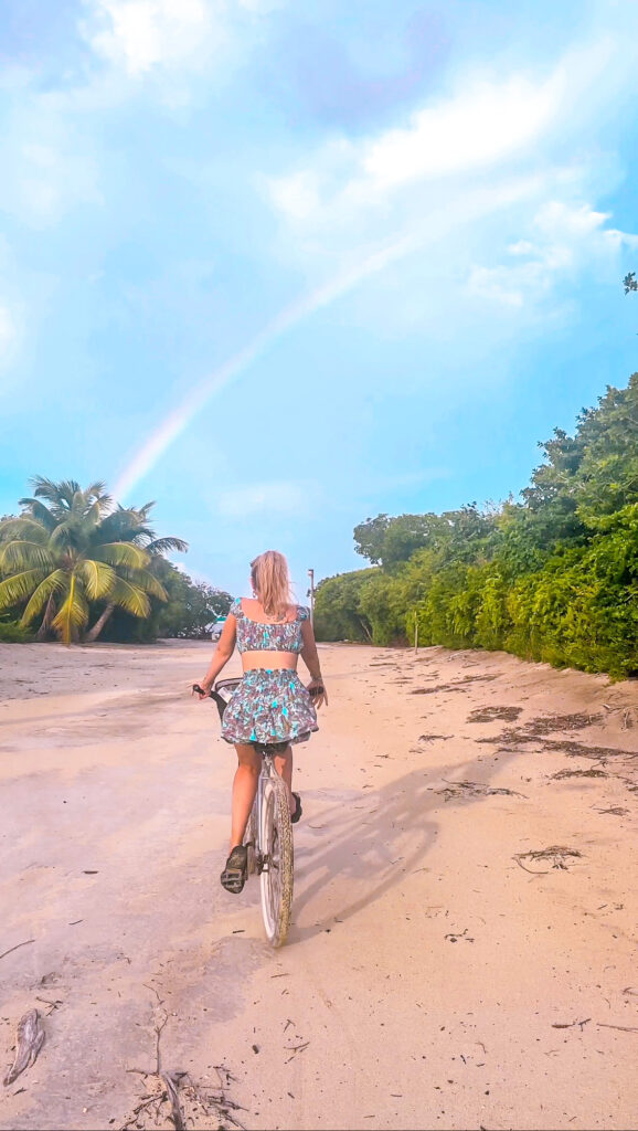 blonde-woman-riding-bike-on-caye-caulker-under-rainbow-on-roomantic-caribbean-getaway
