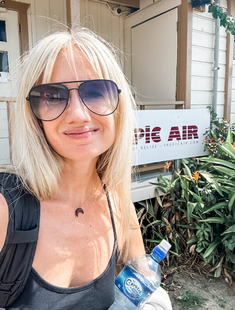 smiling-blonde-woman-with-bangs-holding-water-bottle-in-front-of-tropic-air-sign