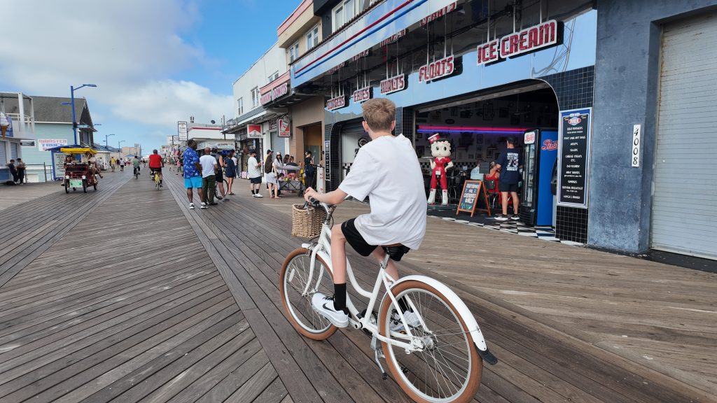 A teenage boy biking on the boardwalk alongside a restaurant with Betty Boop in front of it in Wildwood NJ