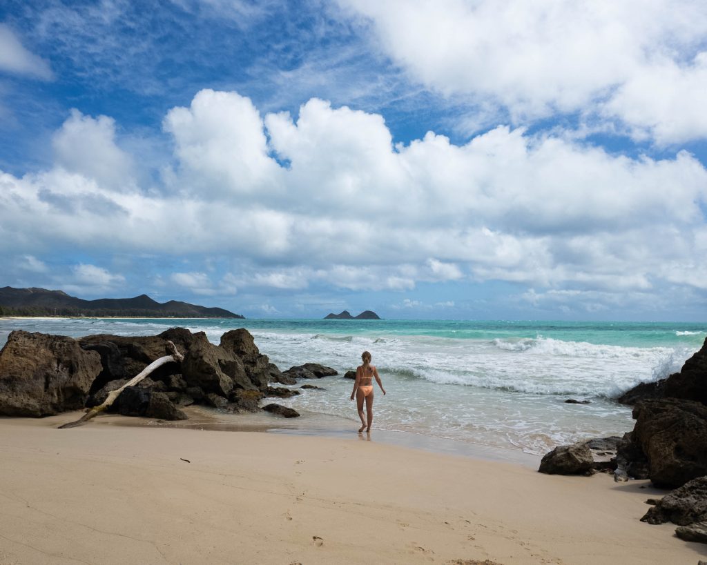 A woman in a peach bikini walking between rocks on a secluded beach with turquoise water