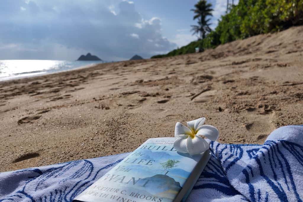 Build The Life You Want Book on a beach towel with a Hawaiian flower and palm trees in the background