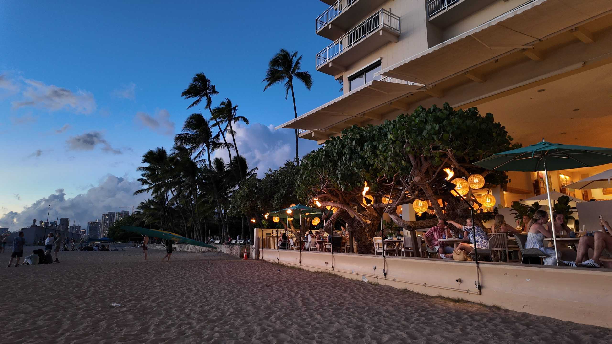 A view from the sand looking towards Hau Tree restaurant in the evening with people eating at it.