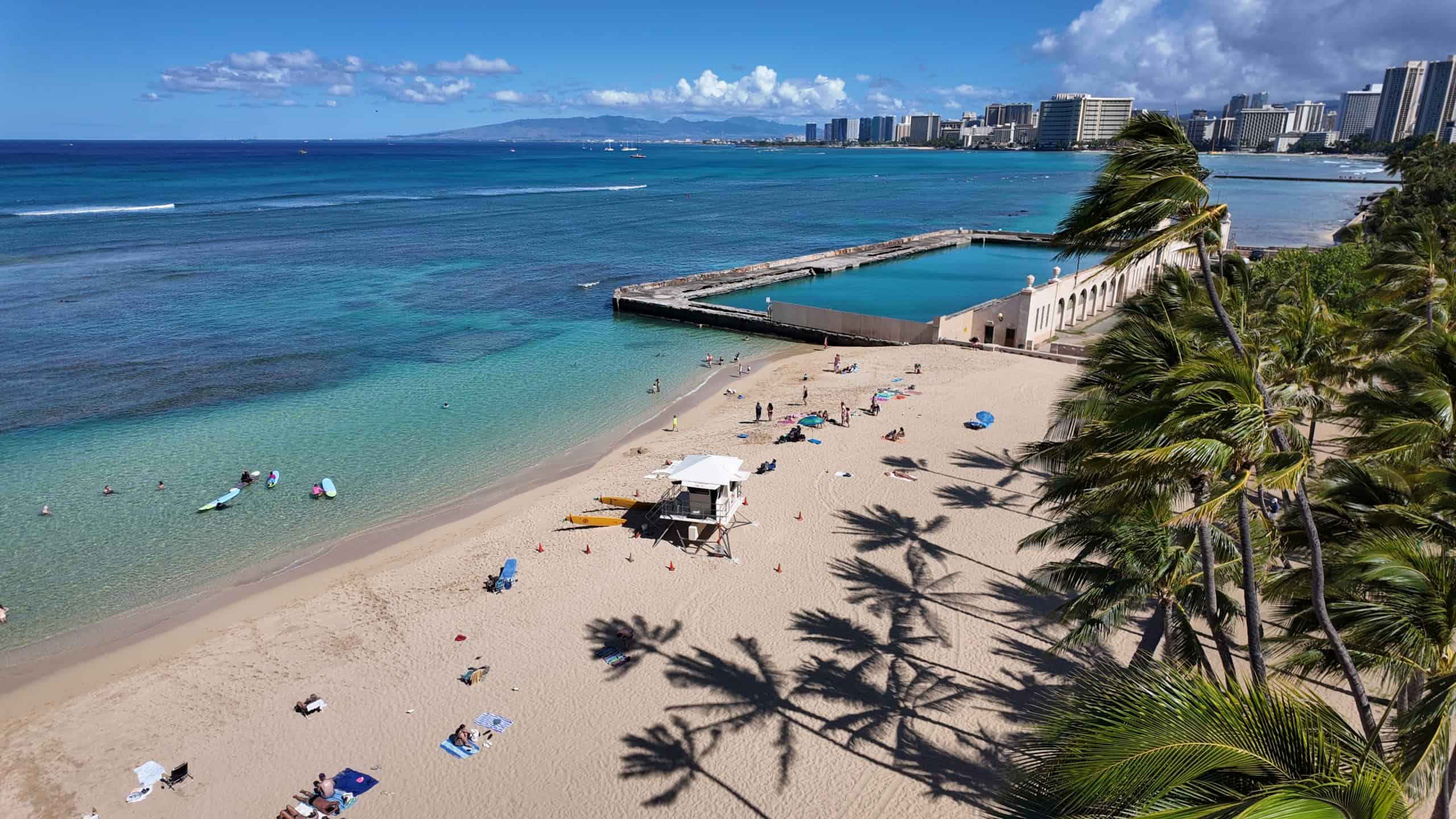 Aerial view of Kaimana Beach and Waikiki, with clear turquoise water, sand, and surfers enjoying the waves near Oahu’s south shore.