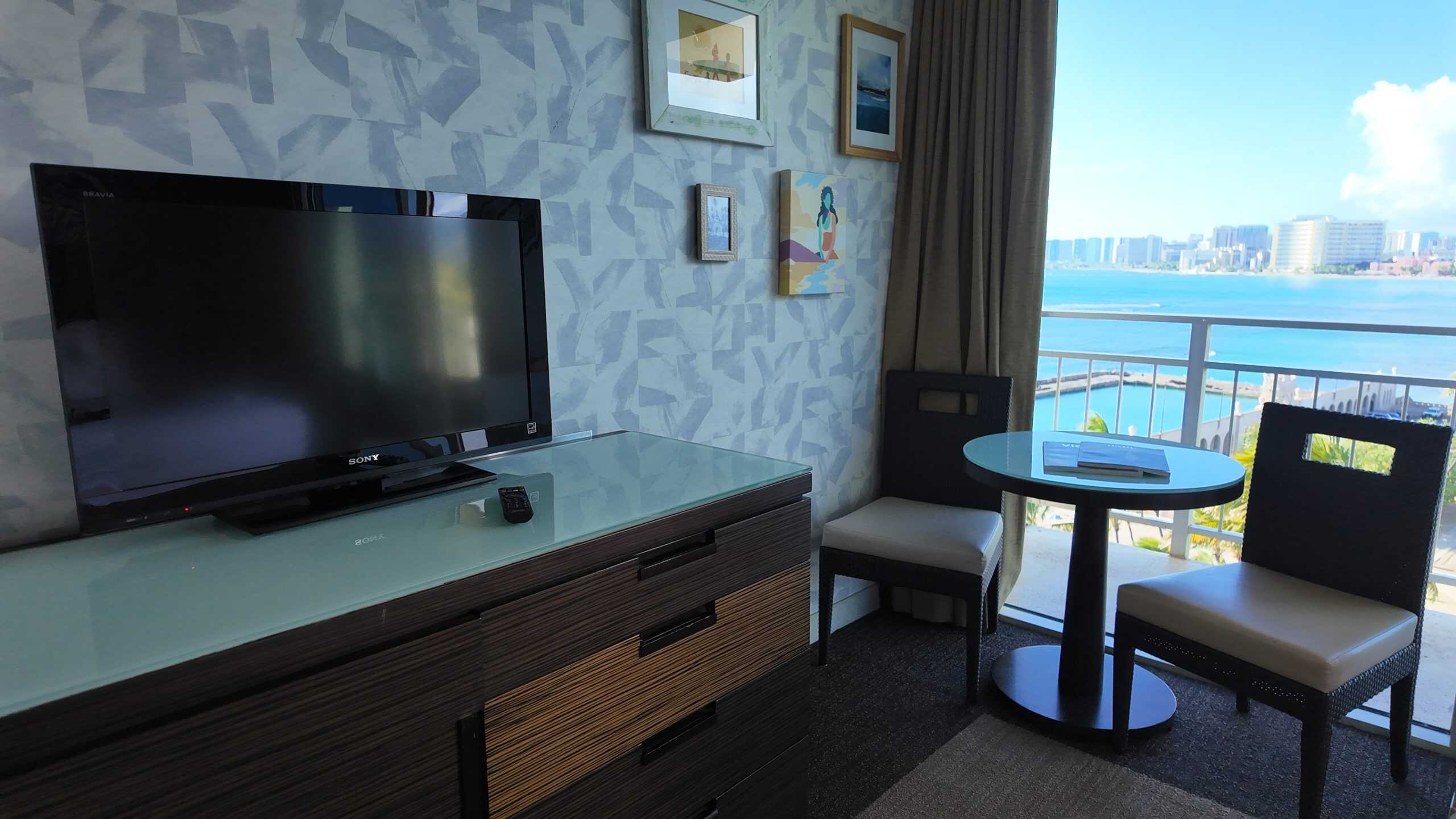 A TV and dresser with a tropical view in the background.