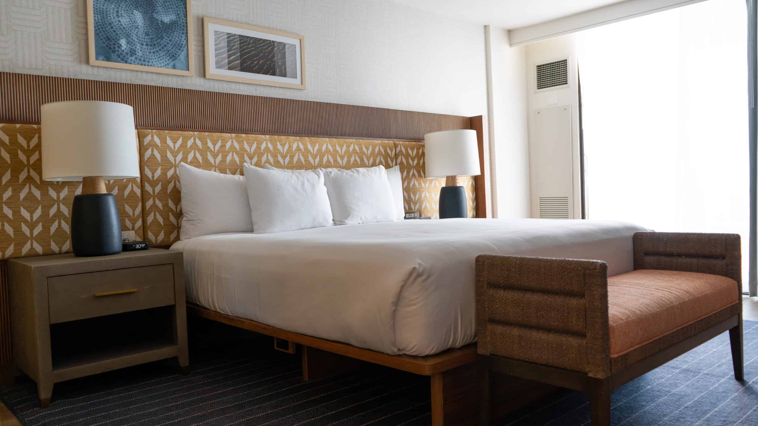 A modern hotel bedroom showing a king sized bed with white linens and light Hawaiian touches