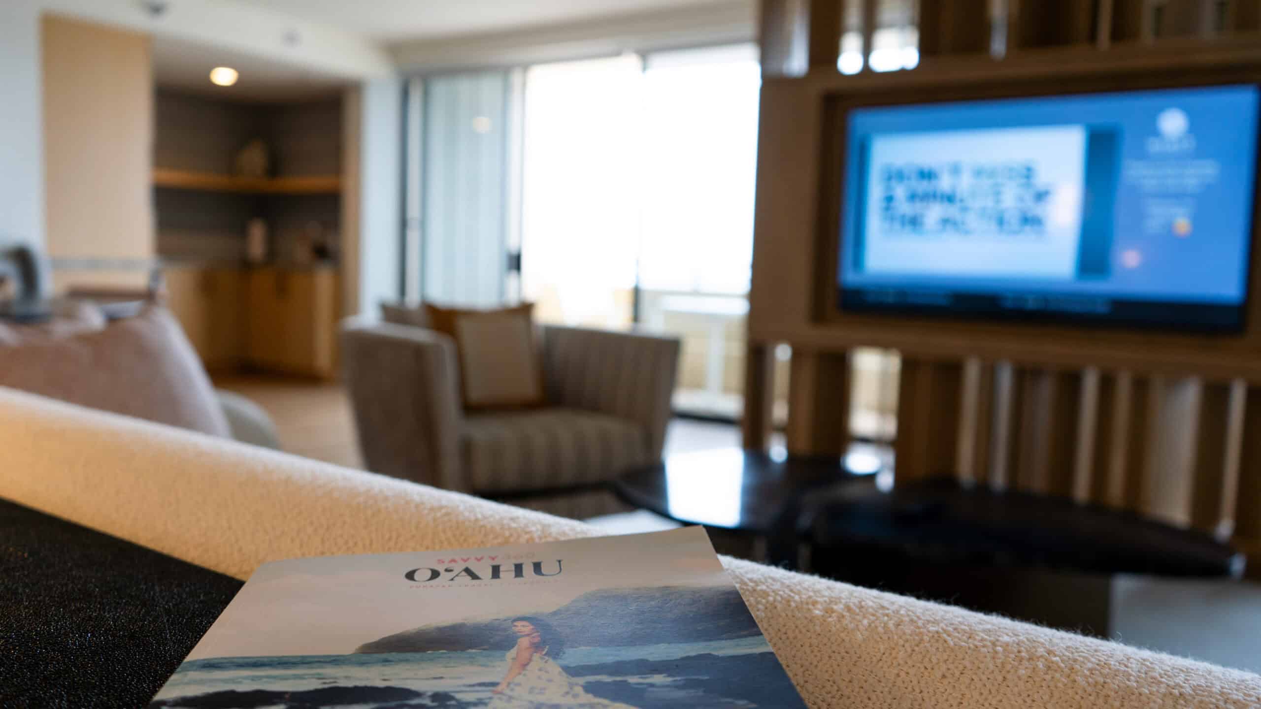 An Oahu magazine looking out at a hotel room suite with a chair and tv