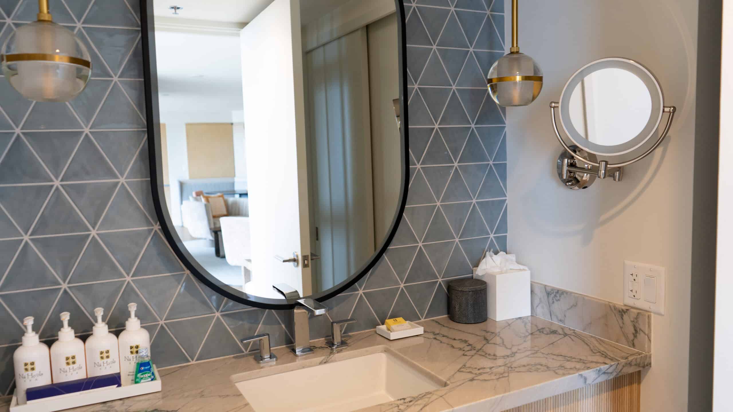 A bathroom with blue tiles, a huge mirror and modern fixtures