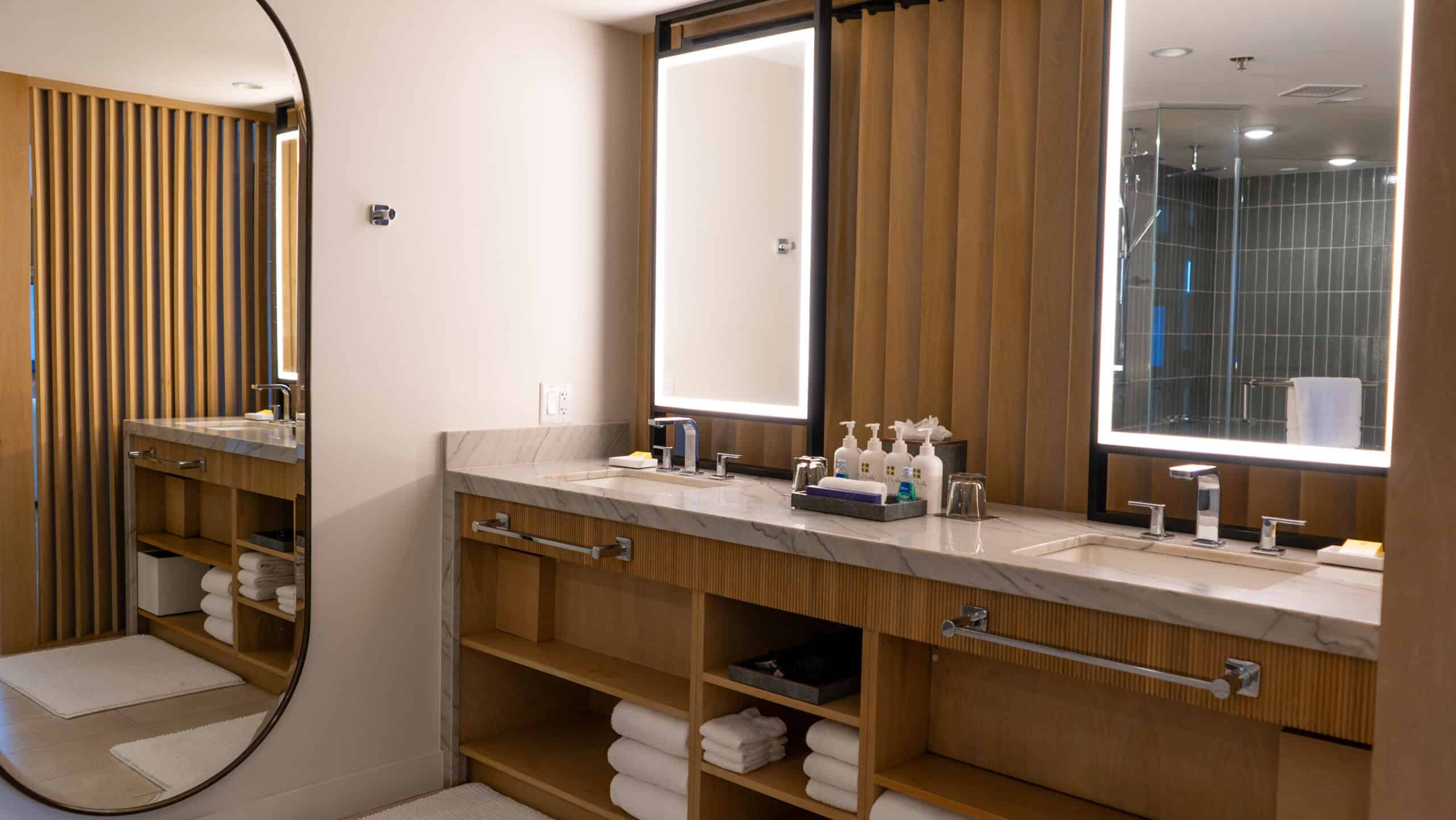 A modern hotel bathroom  at Hyatt Regency Waikiki Beach showing wooden shelving, white towels and spa bath products on the counter