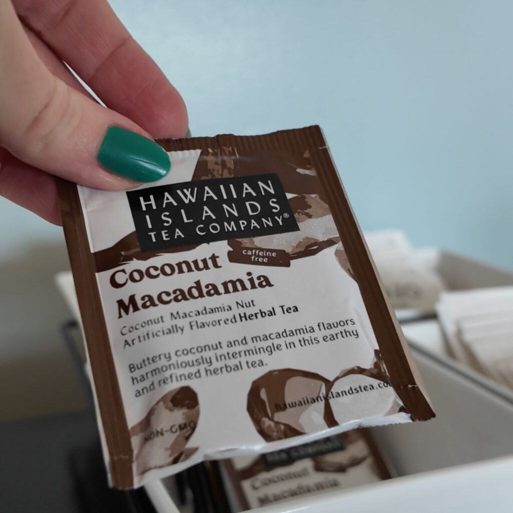 A woman with green nails holding a Coconut Macadamia tea bag.