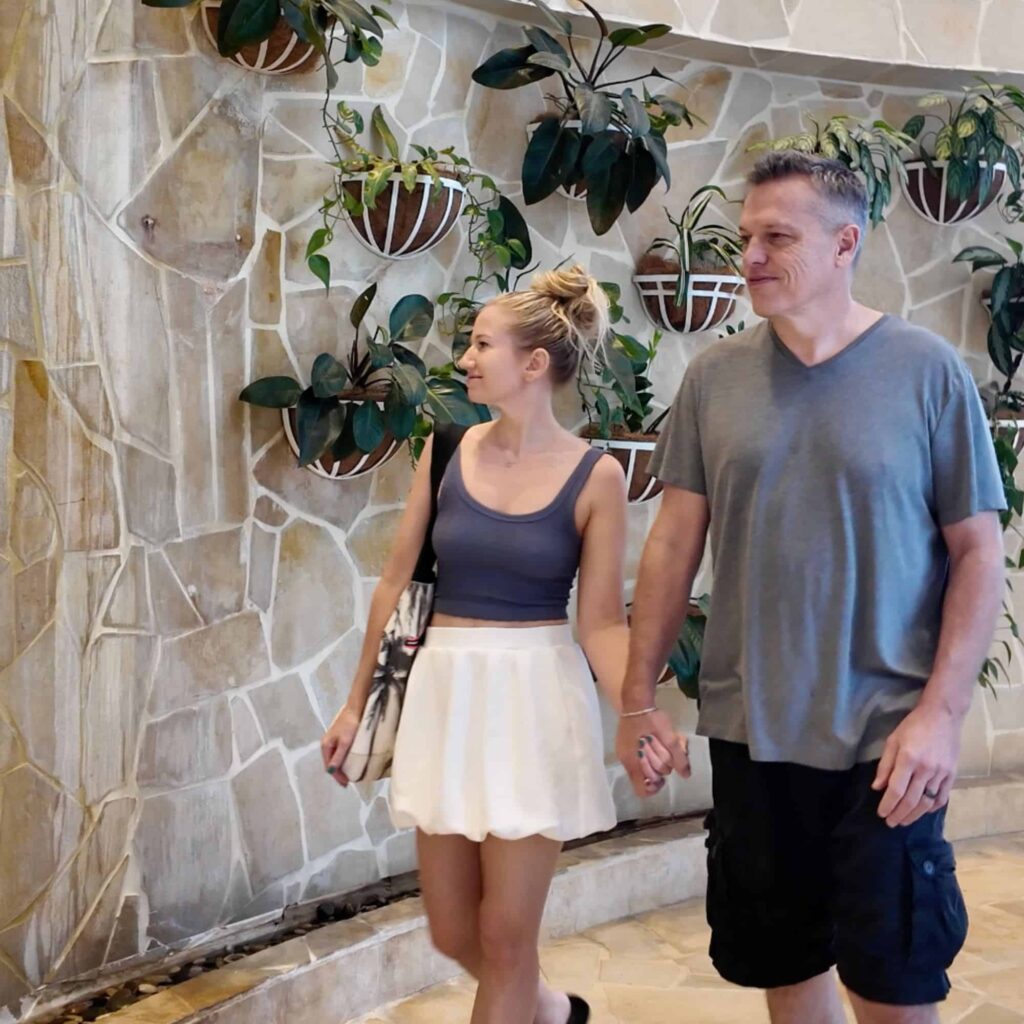 A man and woman walking in front of a wall with plants