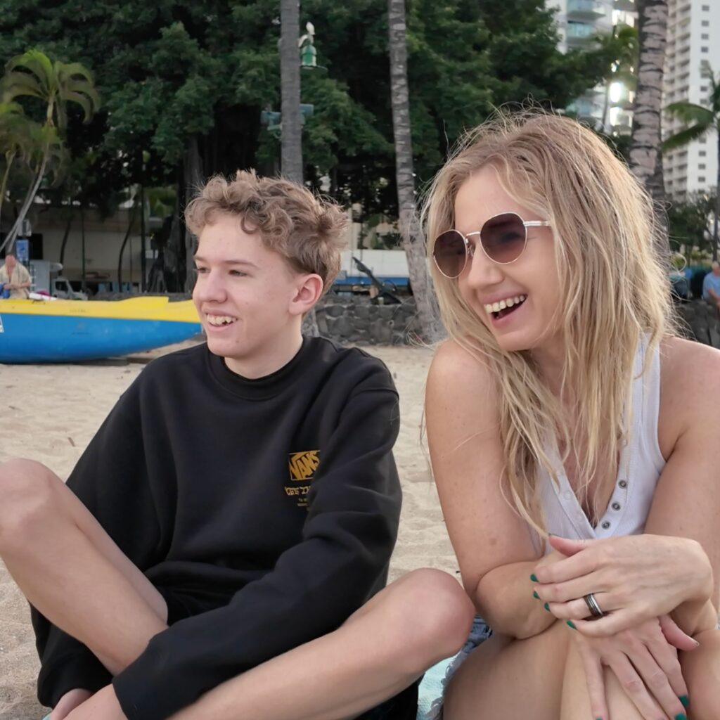 A teen and blonde woman sitting on a beach laughing