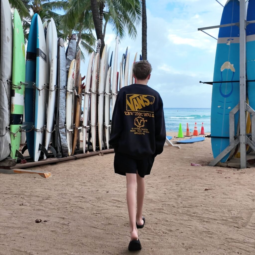 A man in a black vans shirt walking through surfboards towards the ocean