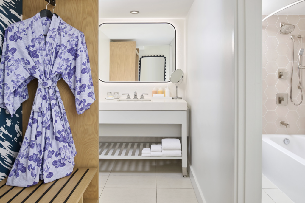 A spacious hotel bathroom with a blue and white kimono style robe, white sink and shelving and a large mirror