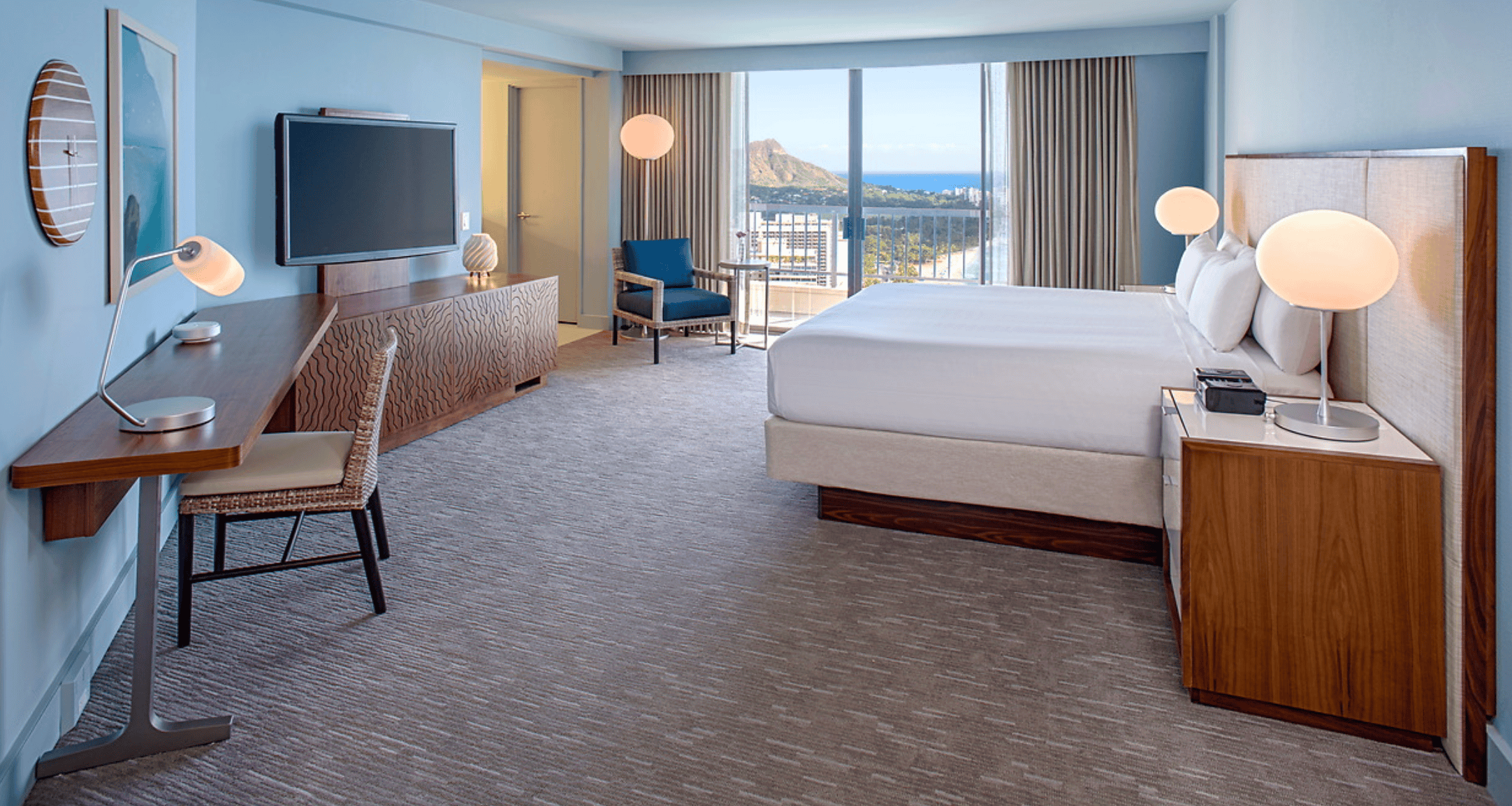 A large standard hotel room at Hyatt Regency Waikiki with a white king bed, light blue walls and a view of Diamond Head
