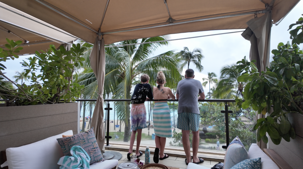 A teenage boy, mom and dad looking over a patio at Waikiki Beach from a hotel patio