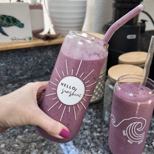 A woman holding a berry almond butter smoothie in a glass jar that says hello gorgeous