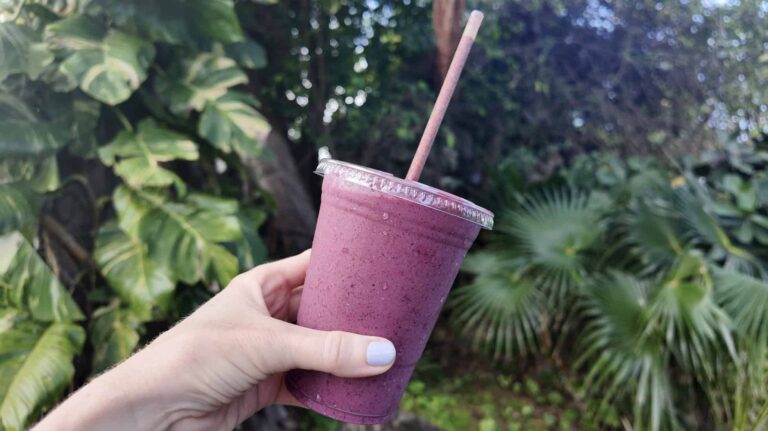 A pink berry almond butter smoothie in front of tropical plants in St. Thomas