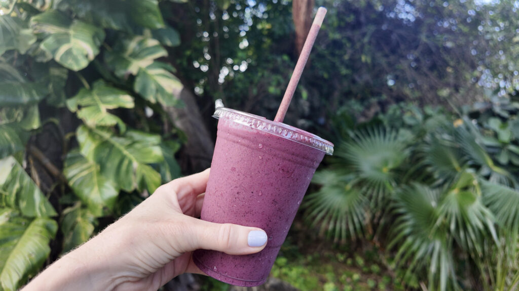 A pink berry almond butter smoothie in front of tropical plants in St. Thomas