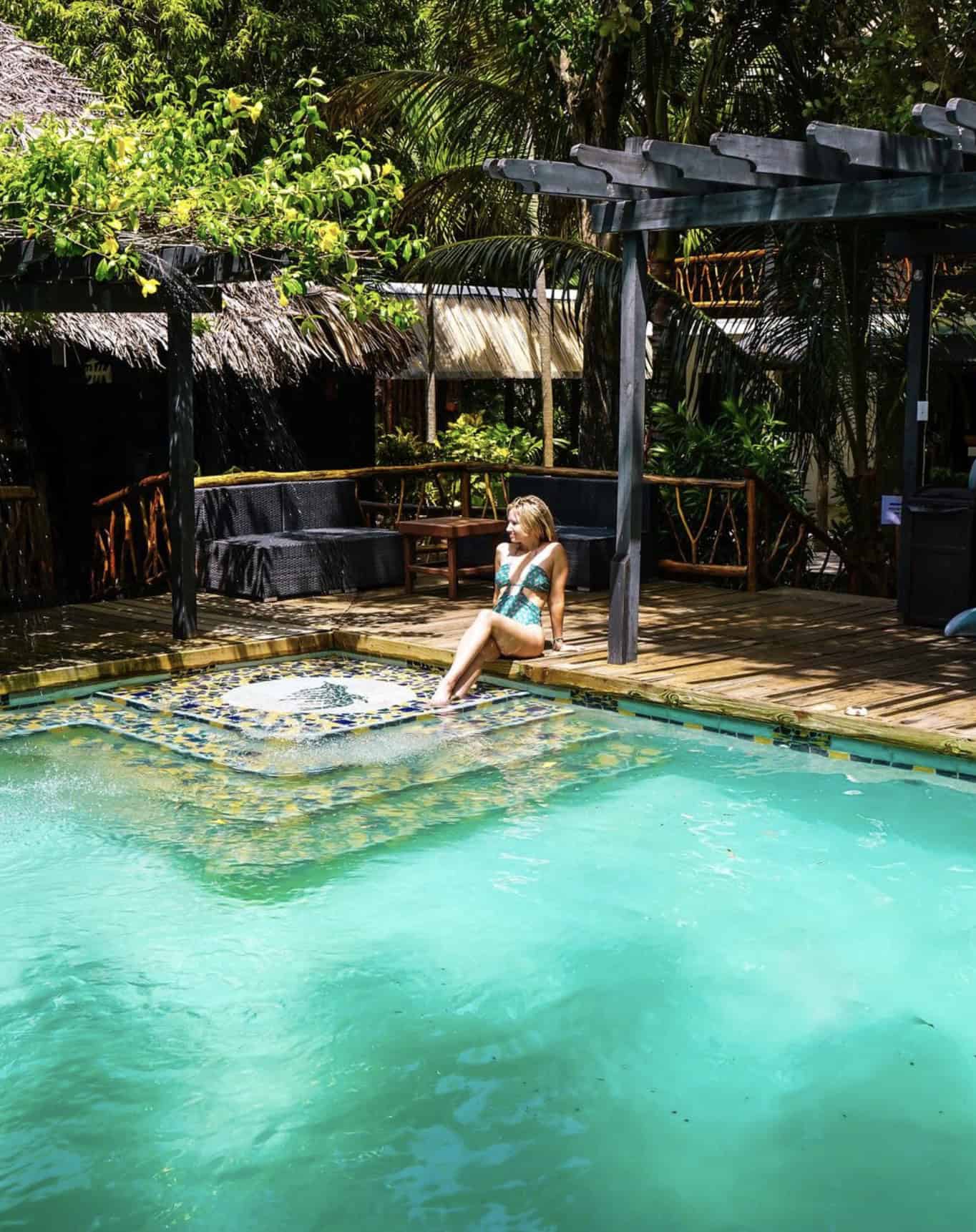 Jenny White sitting by a pool in Belize surrounded by tropical plants