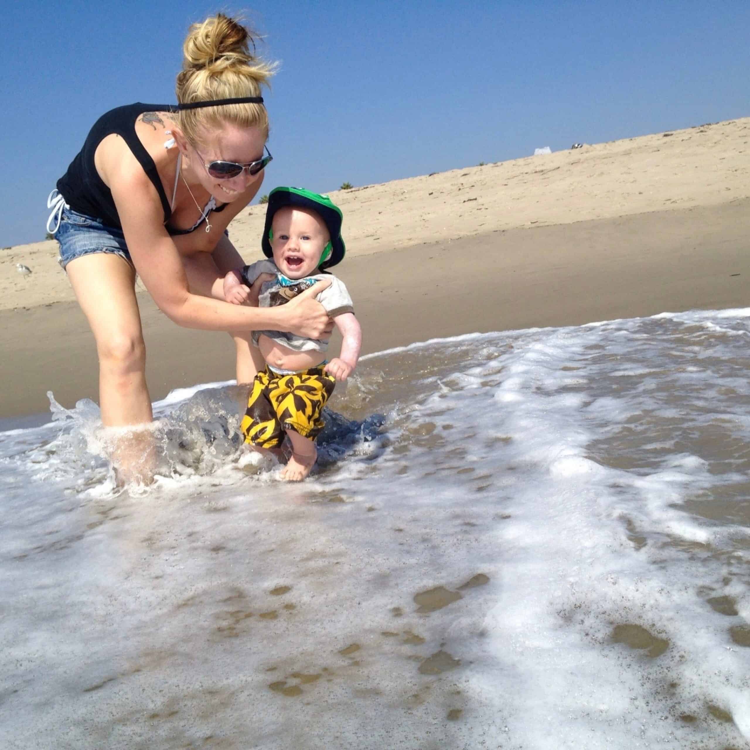 A blonde woman holding a small boy in the ocean waves