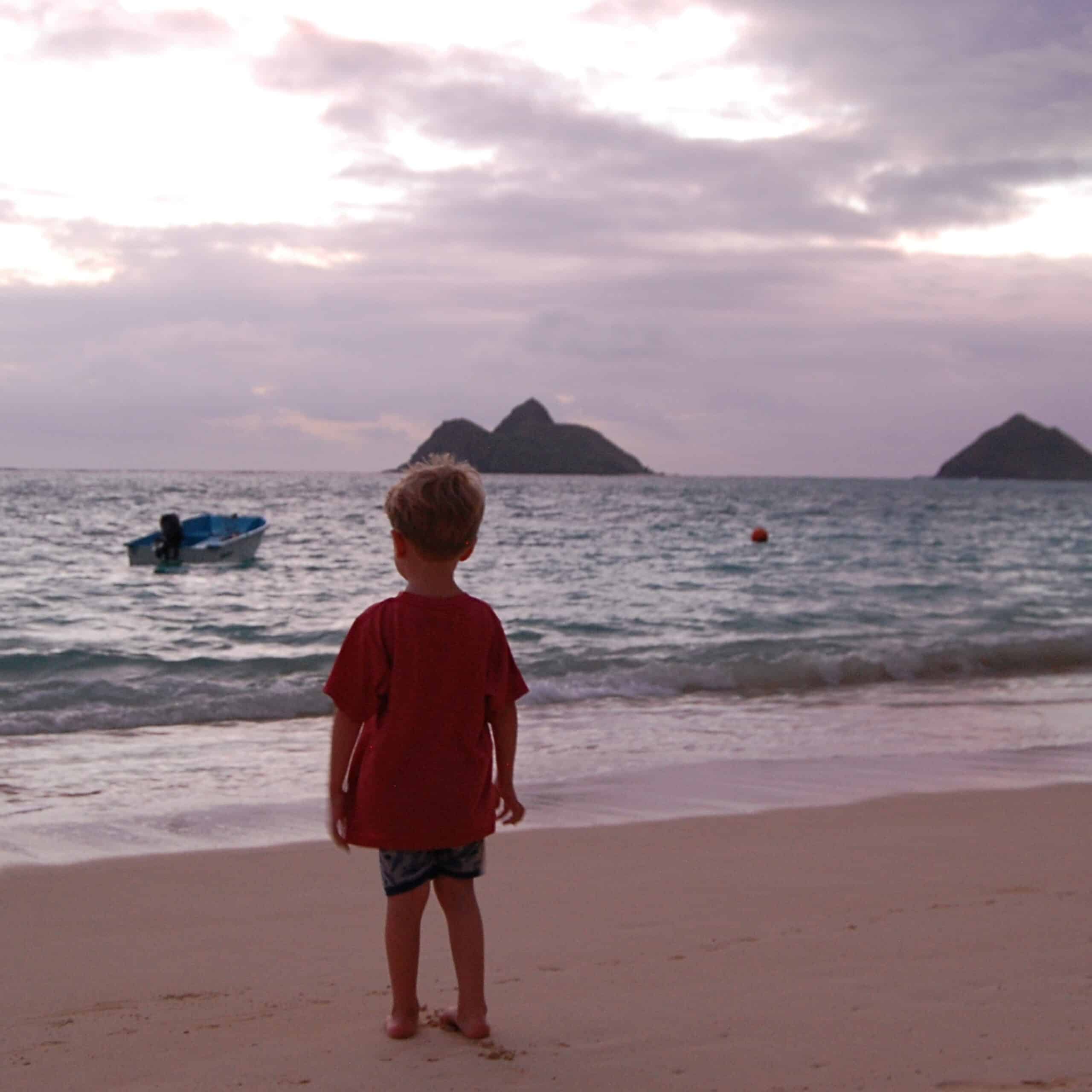 A little boy looking out to the islands off of Lanikai Beach in Oahu at sunrise