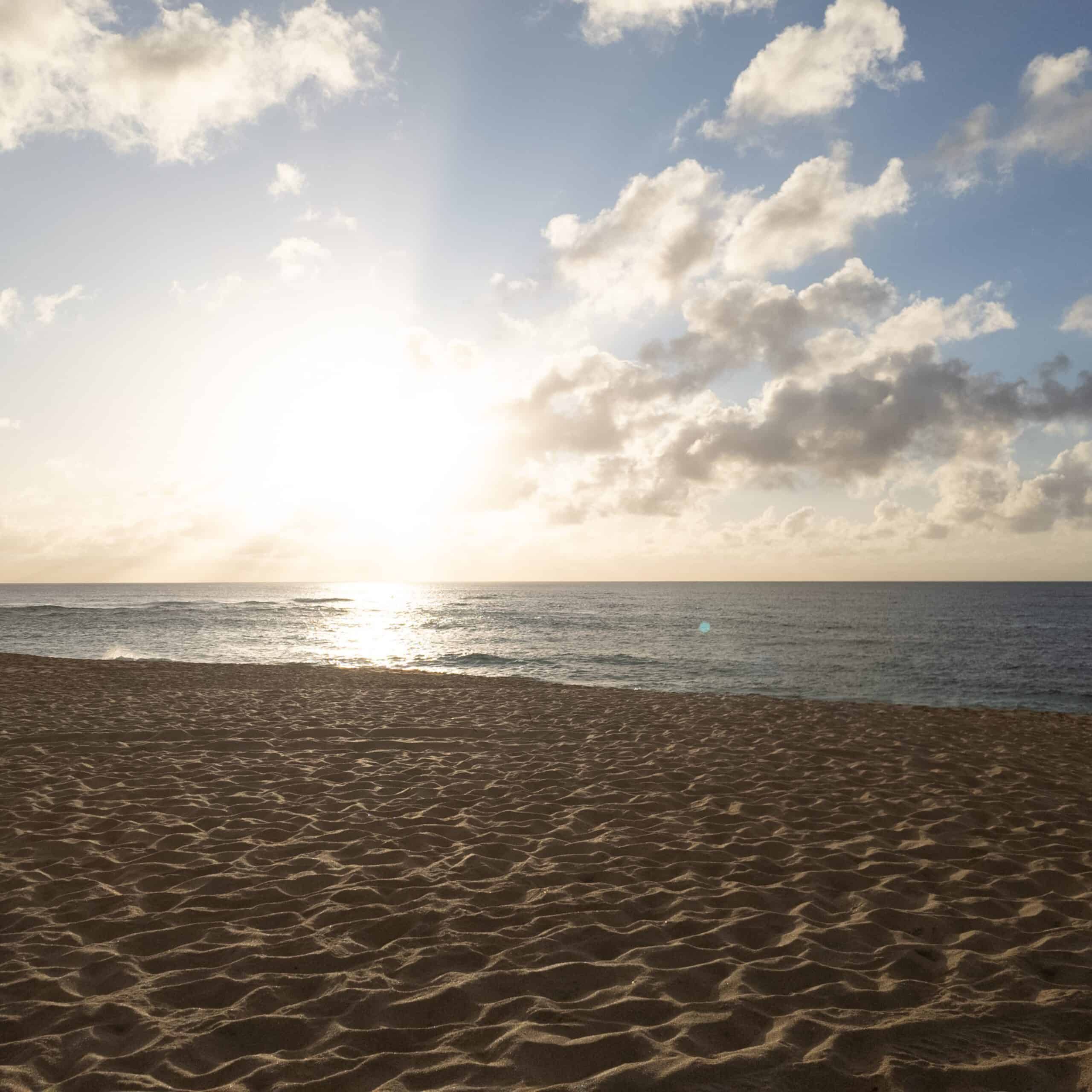 The sun setting over the ocean with fluffy clouds in the sky