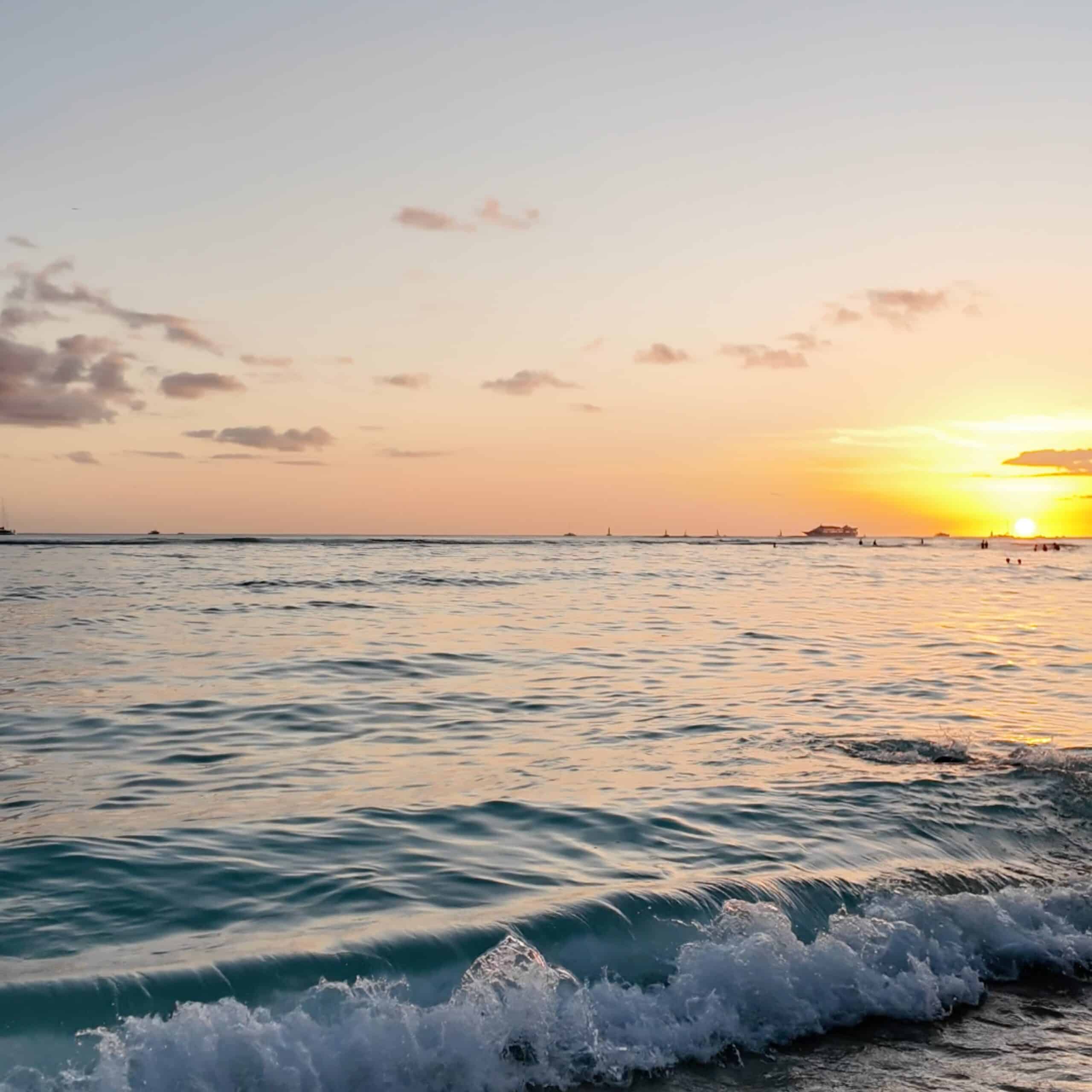 The sun setting off the ocean with waves in the foreground