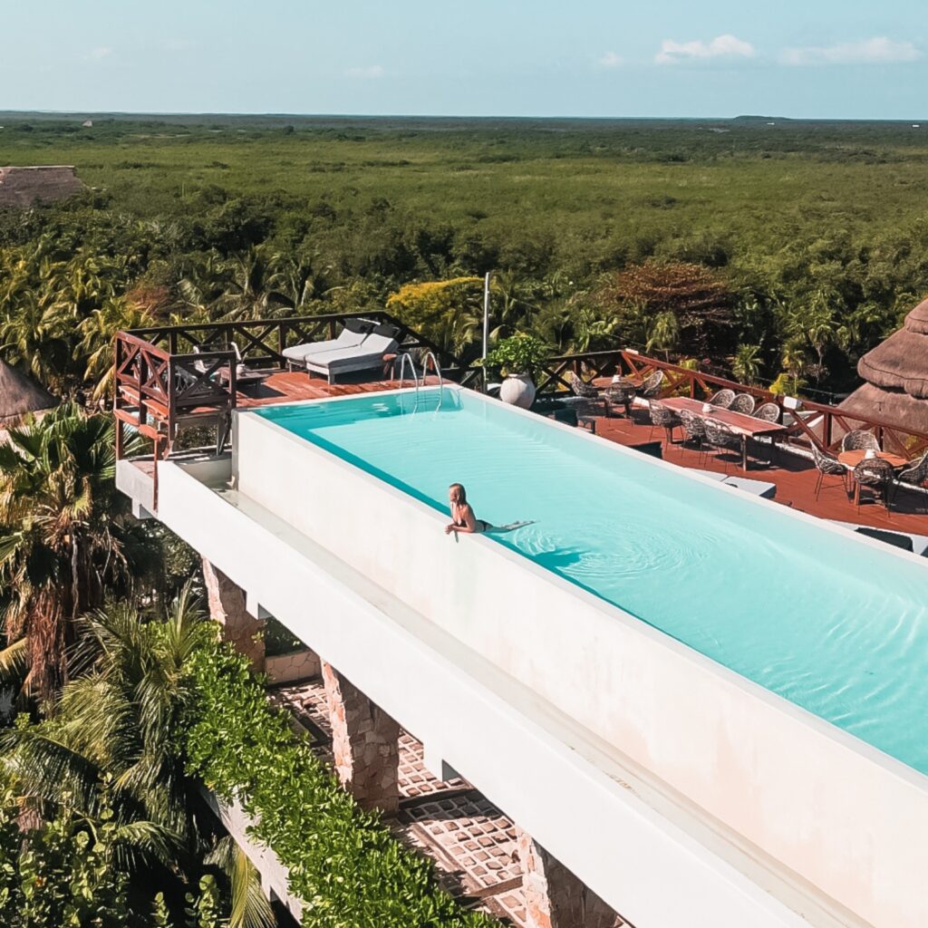 A blonde woman in a stunning luxury hotel pool in Tulum overlooking the beach and ocean