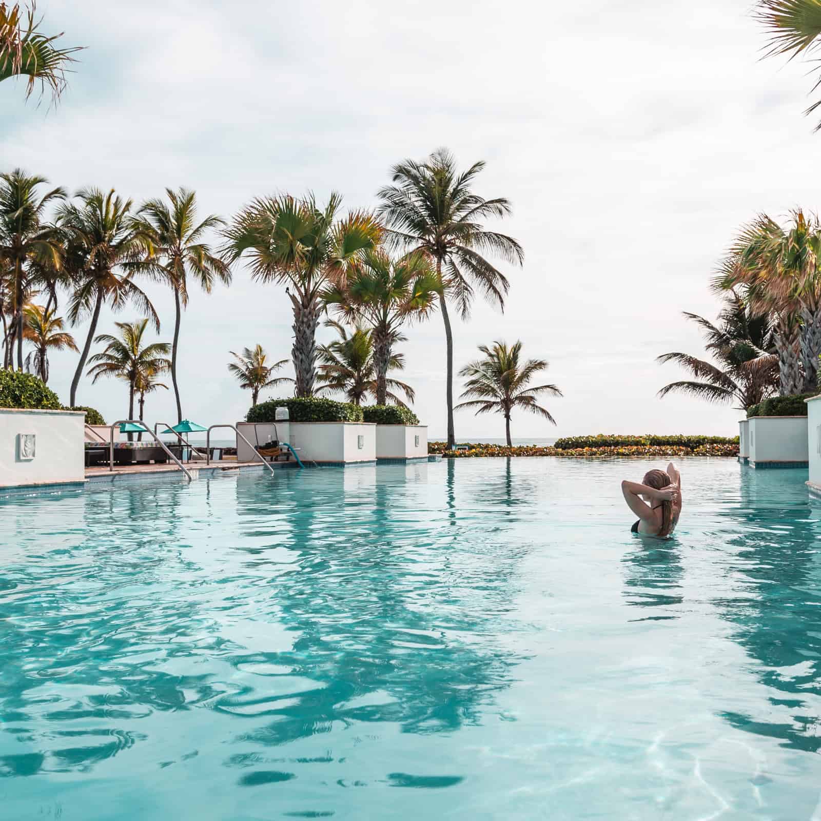 A blonde woman rejuvenating in a tropical hotel pool surrounded by palm trees
