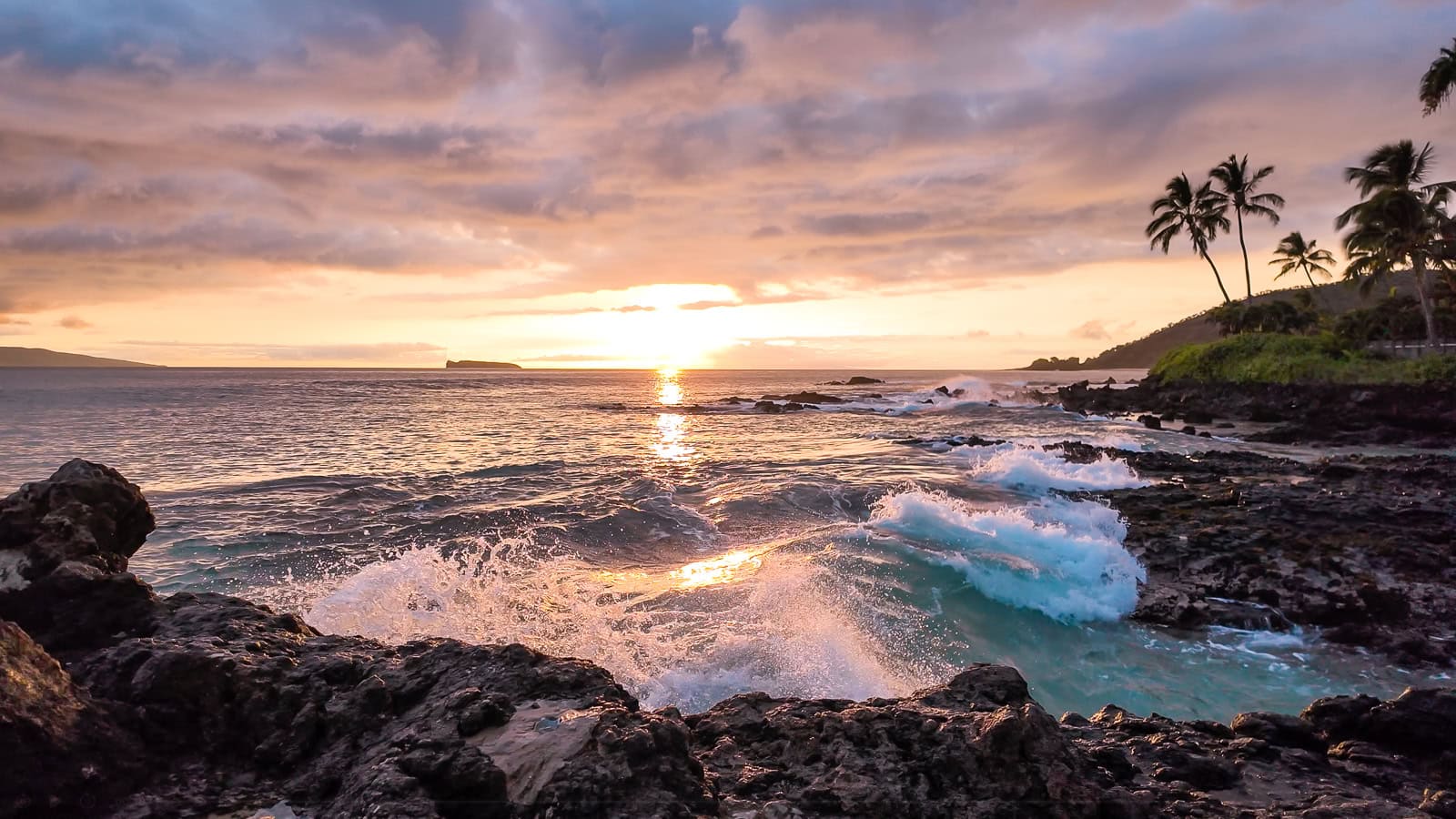 The sun setting over a dramatic view from the shores of Secret Cove in South Maui with turquoise waves in the foreground