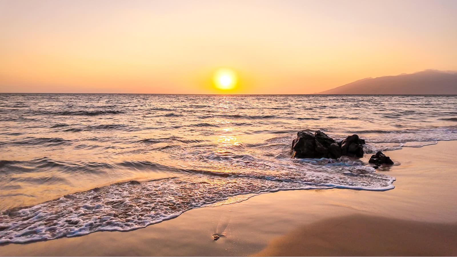 The sun on the horizon setting over the water at Keawakapu Beach in Maui on a clear night