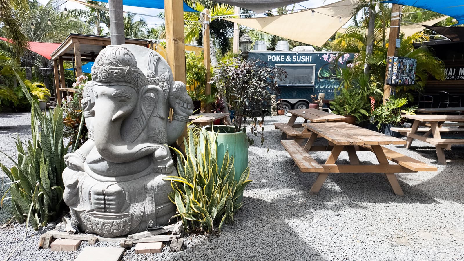 A Ganesha statue with picnic tables and food trucks in the background at Kihei Food Oasis