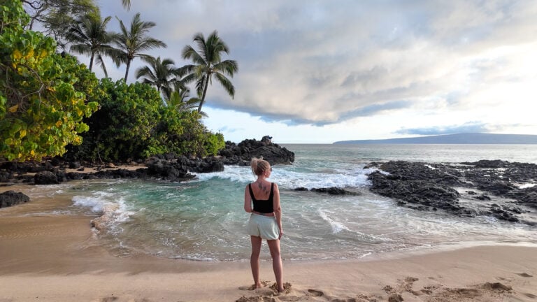 Yoga teacher and travel writer Jenny White standing at the edge of the water on Secret Cove in Maui during golden hour.