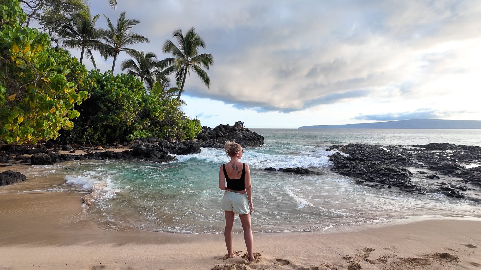 Yoga teacher and travel writer Jenny White standing at the edge of the water on Secret Cove in Maui during golden hour.