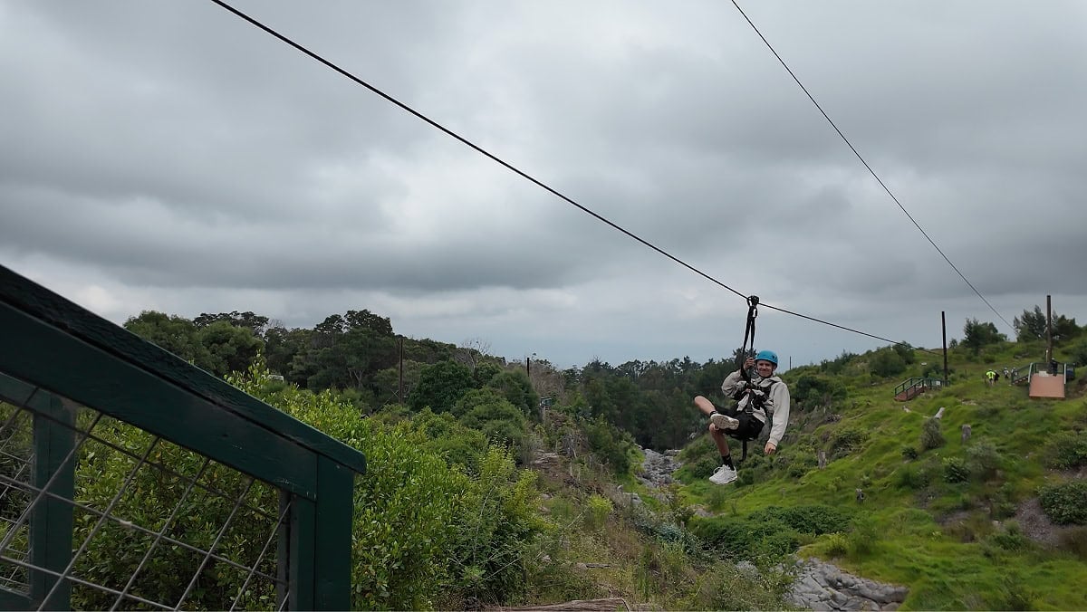 A teen on a zipline smiling at the camera on a gray day in Maui